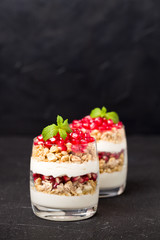 Pomegranate parfait - sweet organic layered dessert with granola flakes, yogurt and fruit seeds on black background.