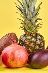 Set of fresh tropical fruits. Delicious pineapple, pomegranate, coconut and mango on yellow background, vertical image.