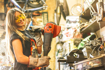 A nice caucasian girl with Angle grinder in workshop with bright light