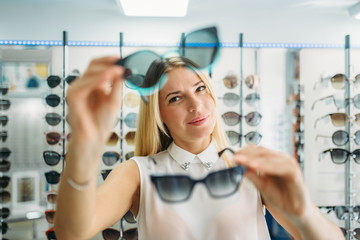 Female buyer chooses sunglasses in optics store