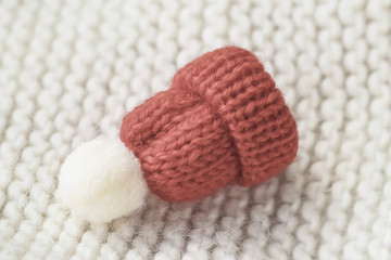 Little knitted decorative red beanie with pompon on a knitted sweater