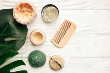 Zero waste flat lay. Natural solid shampoo bar, wooden brush,  deodorant cream, scrub and konjaku sponge on white wood with green monstera leaves. Eco products plastic free