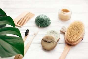 Fototapeta na wymiar Zero waste solid shampoo bar, bamboo toothbrushes, wooden brush, natural deodorant and konjaku sponge on white wood with green monstera leaves. Eco natural products plastic free