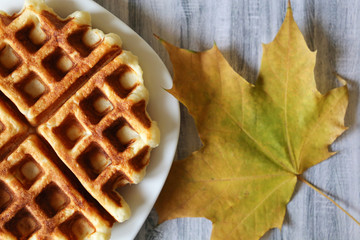 Plate with belgian waffles and autumn maple leaf on wooden table. Fresh homemade dessert