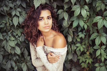 Portrait of young beauty curly latin woman posing near leaves wall on the street