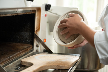 Junge Bäckerin gibt den frischen Teig in den Brotbackofen um gesundes Brot zu backen