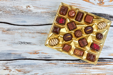 Variety of chocolate candies in box. Variation of delicious truffles in golden box on wooden background and copy space, top view.