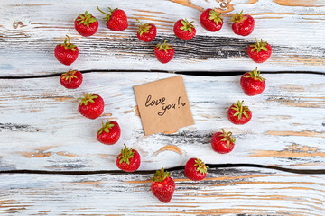 Heart shape from strawberries on wooden background. Juicy berries arranged in a shape of heart. Romantic message on wooden background.