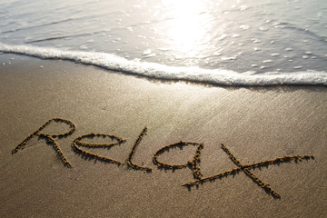 relax written in the sand with incoming wave