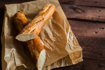 Fresh baguetteon paper bag, on wooden table, close up