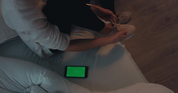 Attractive sporty young Caucasian woman getting ready for exercising early in the morning, tying her sports shoe. GREEN SCREEN. 4K UHD