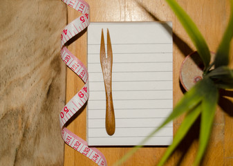 notebook with wooden fork and measuring tape on wooden table