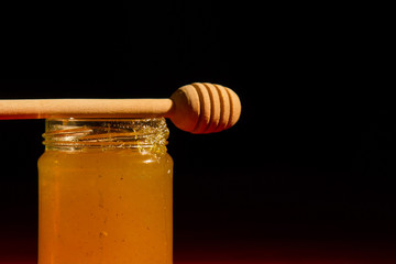 Honey with dipper on wooden background with the the play of light and shadow