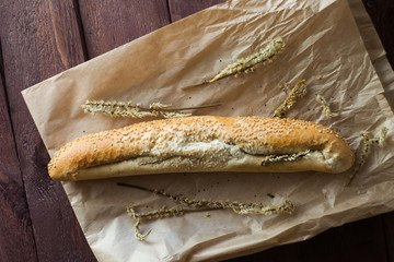 French baguettes with sesame seed on a paper bag lie on a wooden table.