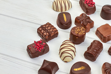 Group of chocolate candies close up. Collection of chocolate sweets on white wooden surface with copy space. Tasty food and calories.