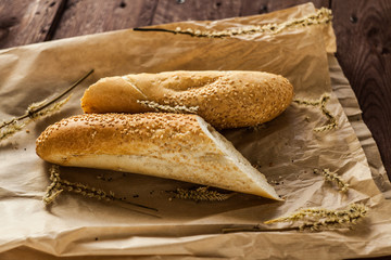 French baguettes with sesame seed on a paper bag lie on a wooden table.