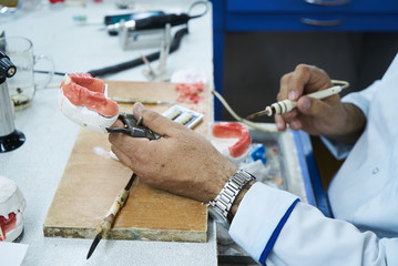 Dental technician using a knife with ceramic dental implants in his laboratory.  Dentist working with tooth dentures in his lab office 