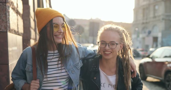 Close up of the two Caucasian happy girls walking the city together in hugs as being best friends and laughing. Outdoors.