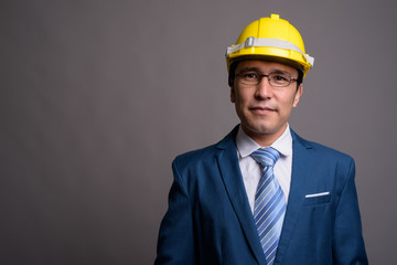 Young Asian businessman wearing hardhat against gray background