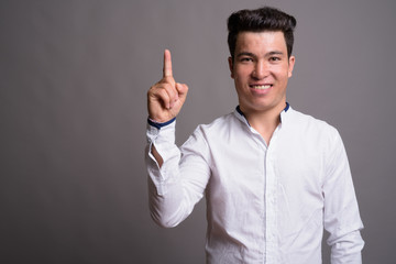 Portrait of young Asian businessman against gray background