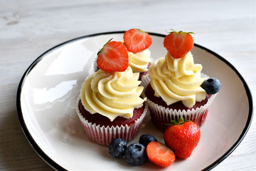 Delicious plate of cupcakes with berries on white wooden surface. Red velvet cupcakes.