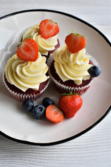 Delicious plate of cupcakes with berries on white wooden surface. Red velvet cupcakes.