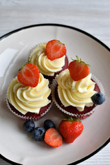 Delicious plate of cupcakes with berries on white wooden surface. Red velvet cupcakes.