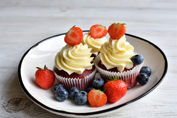 Delicious plate of cupcakes with berries on white wooden surface. Red velvet cupcakes.