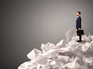 Thoughtful young businessman standing on a pile of crumpled paper with a deep grey background