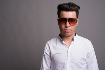 Young Asian businessman wearing sunglasses against gray backgrou