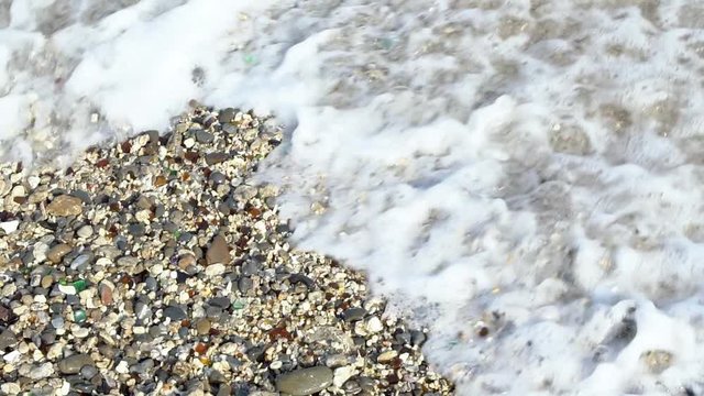 Slow Motion of ocean beach of peebles with the foam of the waves in motion at Taiwan Island. Sea surfs are splashing on multi colored polished stones. The wave on the shore-Dan