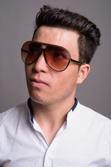 Young Asian businessman wearing sunglasses against gray backgrou