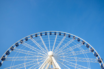 Low angle view of white structure and blue cabin of Ferris wheel with background of clear blue sunny sky.