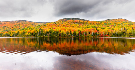 Naklejka premium Fall colors of Lac Legault with Mont Kaaikop in the background, in cottage country in the Laurentians, Quebec, Canada.