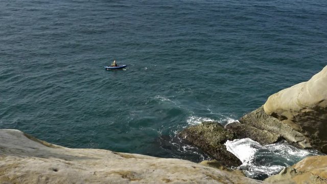 4K, View from the rock of a woman rows an outrigger canoe on still ocean water. Nature Adventure. Scenic of journey in kayak along. Elevated View of people canoeing on sea of Taiwan in Keelung-Dan