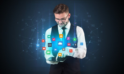 Handsome businessman in suit with tablet on his hand and application icons above
