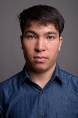 Young Asian man wearing blue shirt against gray background