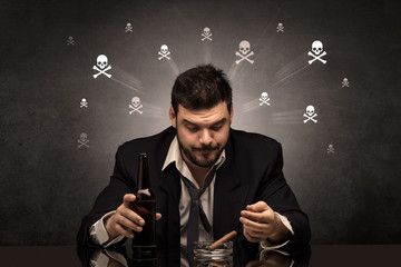 Loser drunk man sitting at table with skulls concept around
