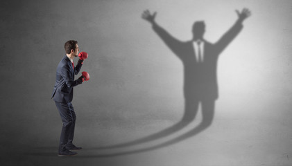 Businessman with boxing gloves fighting with disarmed businessman shadow
