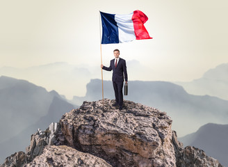 Obraz premium Successful businessman on the top of a mountain holding France victory flag 