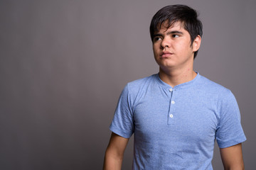 Young Asian teenage boy wearing blue shirt against gray backgrou