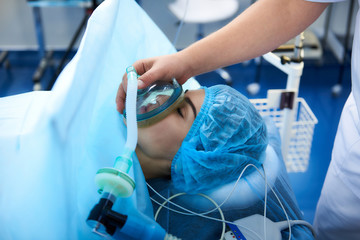 Necessary procedure. Close up of young patient lying with her eyes closed in the operation room and getting narcosis before the surgery - obrazy, fototapety, plakaty
