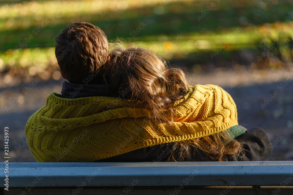 Wall mural the young couple is deeply in love, sitting on a wooden bench enjoying a tender moment in a close em