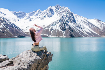 Girl looking at the amazing mountain views of the turquoise waters from the "Embalse del Yeso" (Cast Lake) close to Santiago de Chile city in Andes mountains. Snow mountains and water reflections
