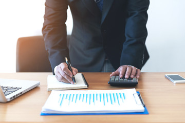 Close up businessman hand using calculator and writing make note with calculate about cost at office.