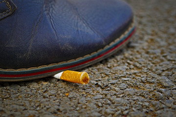 closeup of shoe extinguishing cigarette butt on asphalt