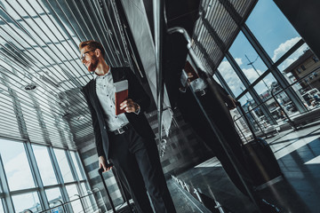 Low angle of a cheerful bearded businessman holding his personal documents while going long the airport