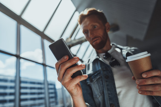 Close up of a smartphone in hands of a baffled man using it while reading shoking news