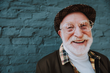 Close up portrait of happy emotional pensioner smiling and standing near gray wall outdoor. Copy...