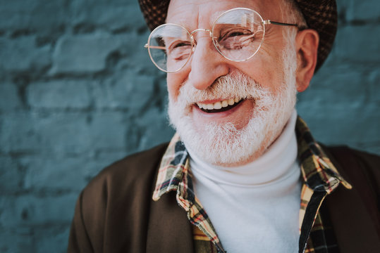 Close up portrait of cheerful pensioner staying near gray brick wall and smiling